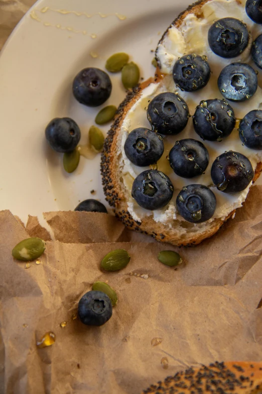 a white plate topped with a bagel covered in blueberries, a portrait, by Leo Michelson, unsplash, seeds, toast, by greg rutkowski, dwell