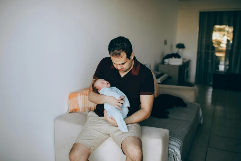 a man sitting on a couch holding a baby, pexels, happening, avatar image, sitting on the bed, 7 0 mm photo, profile picture