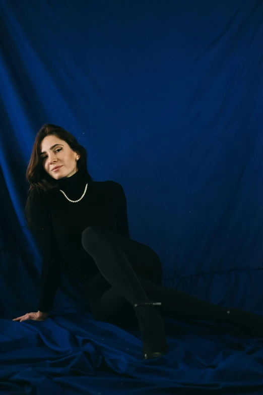 a woman sitting on top of a blue sheet, an album cover, black turtleneck, jen atkin, in a photo studio, dark. no text