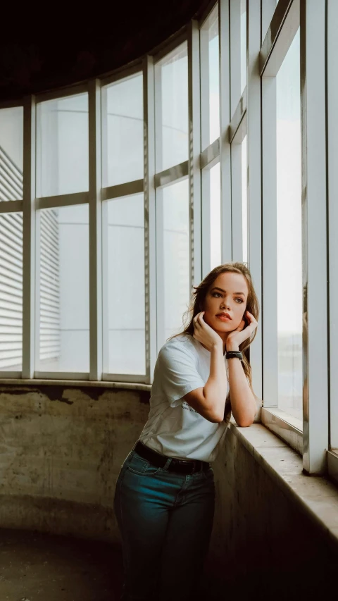 a woman leaning against a window with her hand on her chin, an album cover, inspired by Elsa Bleda, trending on pexels, photorealism, dressed in a white t-shirt, carson ellis, wide forehead, casual pose