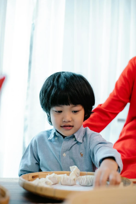 a little boy sitting at a table with a plate of food, ruan jia and brom, playing board games, fatherly, comforting