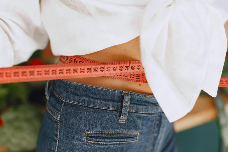 a woman measuring her waist with a measuring tape, by Emma Andijewska, trending on pexels, wearing jeans, brightly coloured, close-up imagery, where a large