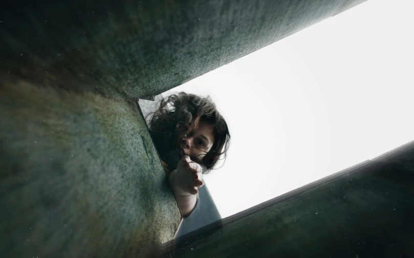 a close up of a person looking out of a window, a picture, claustrophobia, a high angle shot, head tilted down, inside a tomb