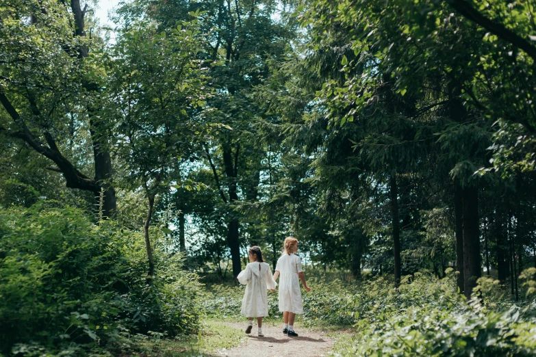 a couple of people walking down a dirt road, inspired by Elsa Beskow, unsplash, arts and crafts movement, dressed in white robes, lakeside, two girls, woodland location