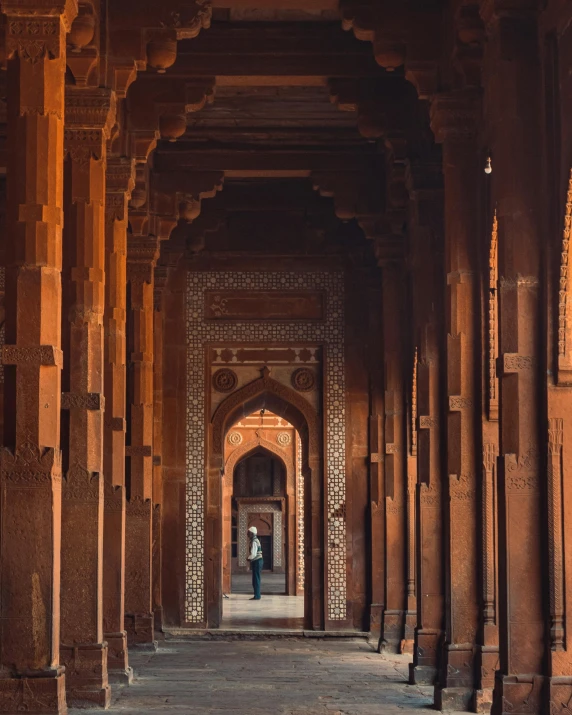 a person walking through an archway in a building, inspired by Steve McCurry, unsplash contest winner, arabesque, with beautiful mosques, ancient india, red bricks, wooden structures