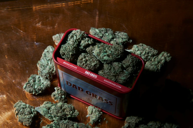 a tin of marijuana sitting on top of a wooden table, red grass, dadaist, baars, lush greens