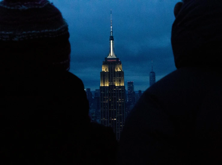 a couple of people that are standing in front of a building, by Adam Rex, pexels contest winner, empire state building, cold top lighting, view from a distance, slide show