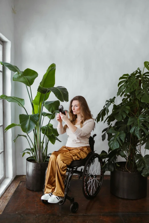 a woman sitting in a wheel chair next to a potted plant, room full of plants, taking a picture, dasha taran, on a gray background