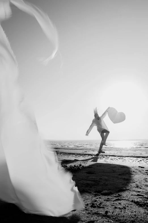 a woman standing on top of a beach holding a surfboard, a black and white photo, by Leo Leuppi, pexels contest winner, girl with angel wings, running freely, winter sun, cupid
