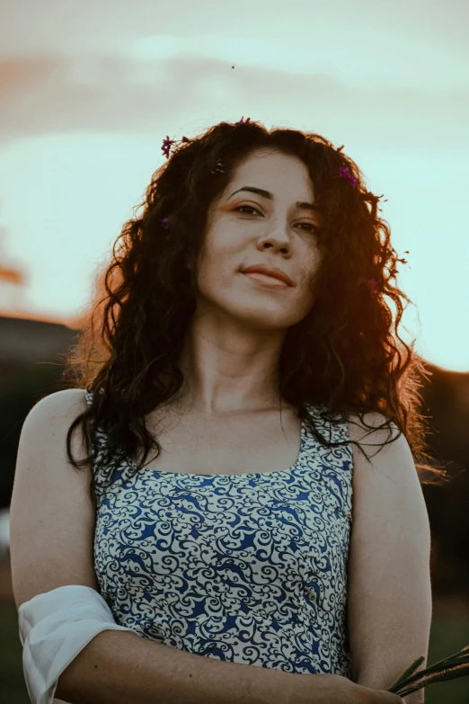 a woman standing in a field holding a bunch of flowers, an album cover, pexels contest winner, (dark shorter curly hair), looking off into the sunset, yael shelbia, concert