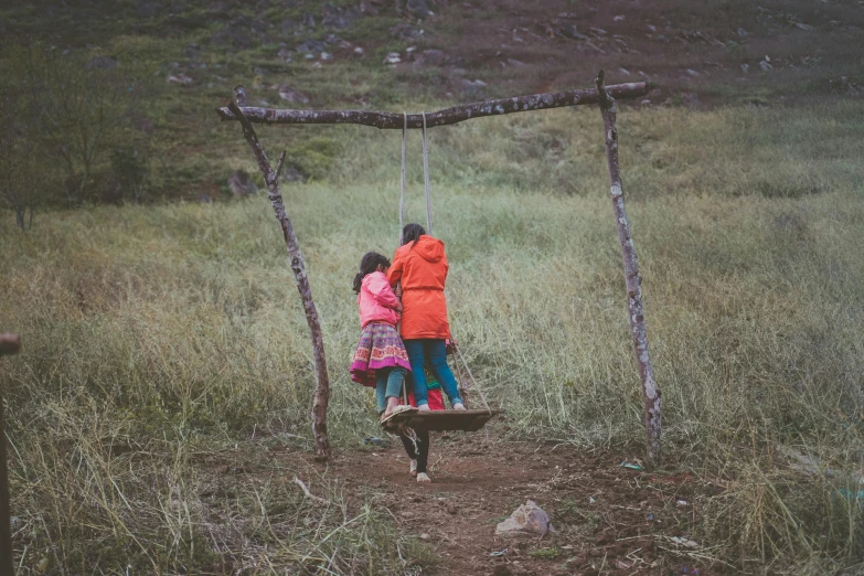 a couple of people on a swing in a field, by Jessie Algie, pexels contest winner, faroe, kids playing, rustic, holding each other