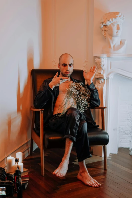 a man sitting in a chair in front of a fireplace, an album cover, inspired by Hedi Xandt, pexels contest winner, aestheticism, shaved head, gothic outfit, provocative indian, handsome man