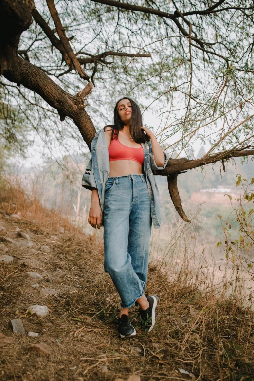 a woman standing on top of a hill next to a tree, baggy jeans, wearing crop top, curated collections, 2 0 yo