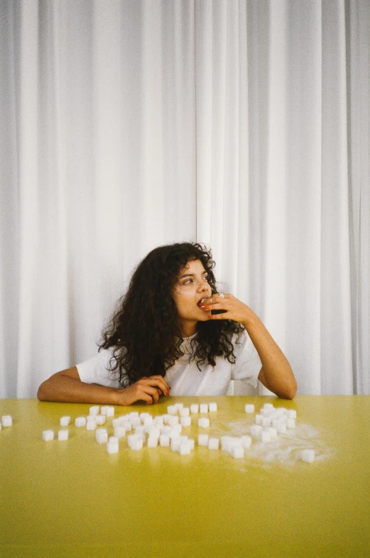 a woman sitting at a table with marshmallows on it, an album cover, asher duran, curly hair, in front of white back drop, ignant