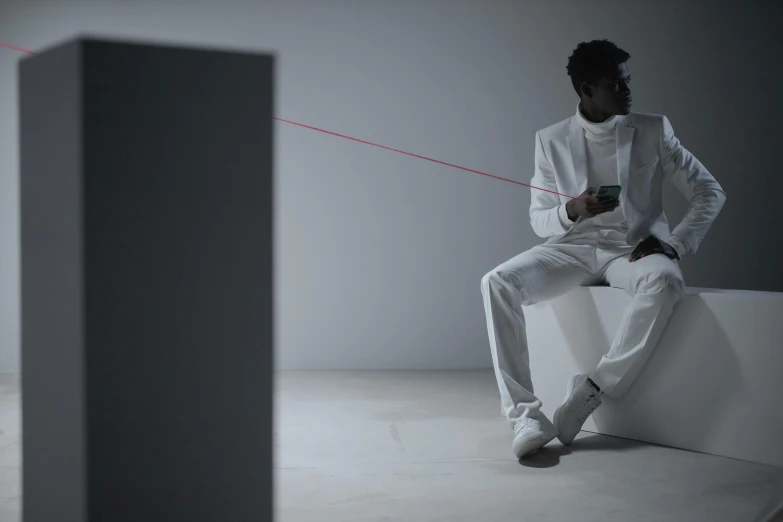 a man sitting on a ledge using a cell phone, inspired by Carrie Mae Weems, video art, thin red lines, white room, vfx render, white suit