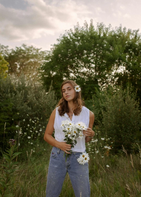 a woman standing in a field holding a bunch of flowers, inspired by Elsa Bleda, dressed in a white t shirt, press shot, mina petrovic, full frame image