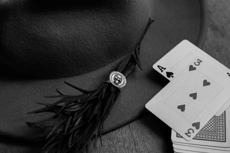 a black and white photo of a hat, playing cards, and a feather, by Emma Andijewska, pexels contest winner, badge on collar, wsop, chrome hearts, enhanced