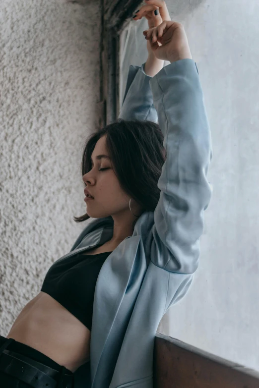 a woman leaning against a wall with her arms in the air, inspired by Elsa Bleda, sport bra and shirt, blue and gray colors, asian women, wearing jacket