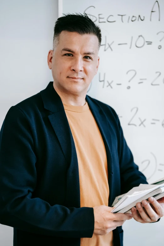 a man standing in front of a whiteboard holding a book, math inspired, 2019 trending photo, portrait shot, lgbtq