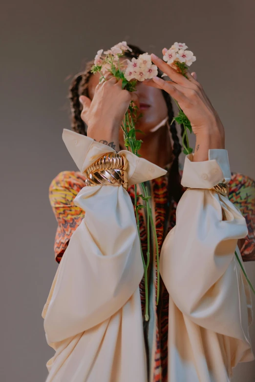 a woman holding flowers in front of her face, an album cover, by Nina Hamnett, trending on pexels, renaissance, ruffles tassels and ribbons, showstudio, leather cuffs around wrists, white sleeves
