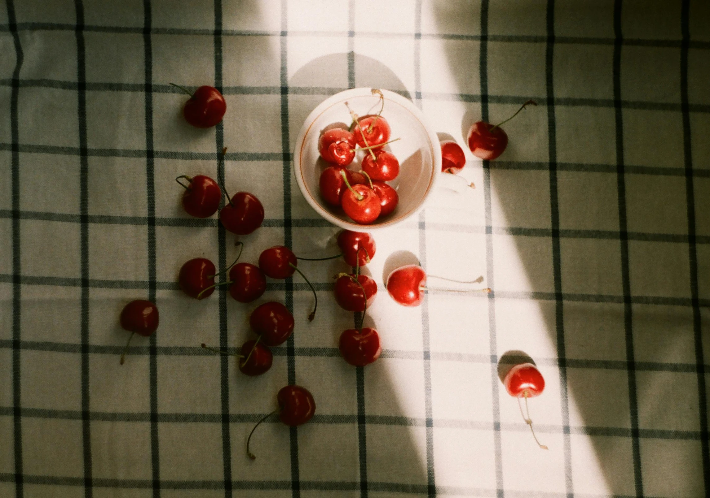 a bowl of cherries sitting on top of a table, inspired by Elsa Bleda, unsplash contest winner, on a checkered floor, sunlight beaming down, ignant, red and white lighting