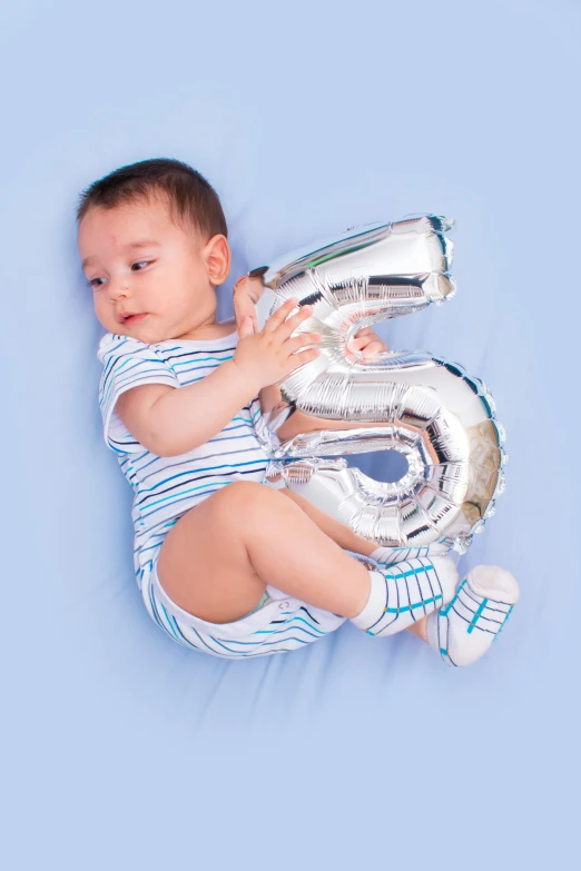 a baby holding a silver number five balloon, shutterstock contest winner, happening, inflatable future shoes, blue themed, age lines, panels