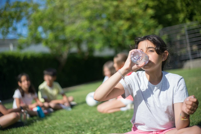 a woman sitting on the grass drinking from a water bottle, by Julian Allen, pexels contest winner, school class, slightly sunny, 15081959 21121991 01012000 4k, instagram post