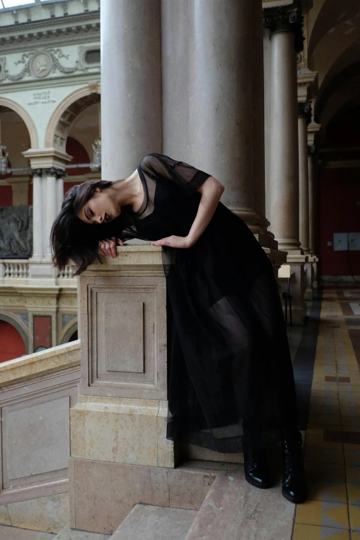 a woman in a black dress leaning on a pillar, inspired by irakli nadar, pexels contest winner, renaissance, in a large hall, at a fashion shoot, tall female emo art student, sheer