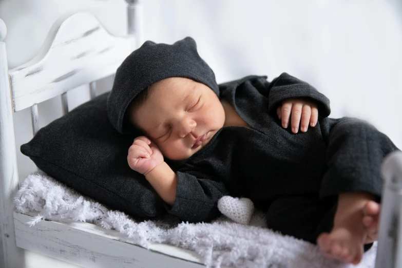 a close up of a baby sleeping on a bed, by Ruth Simpson, pexels contest winner, happening, dressed black hoodie, with index finger, wearing dark grey suit, various posed