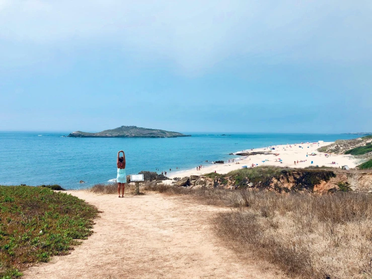 a man standing on top of a sandy beach next to the ocean, by Olivia Peguero, pexels contest winner, panoramic view of girl, a road leading to the lighthouse, hollister ranch, dua lipa