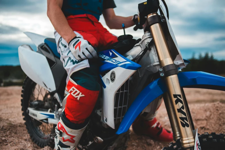 a person that is sitting on a dirt bike, unsplash, photorealism, red and blue garments, avatar image, knee pads, brown