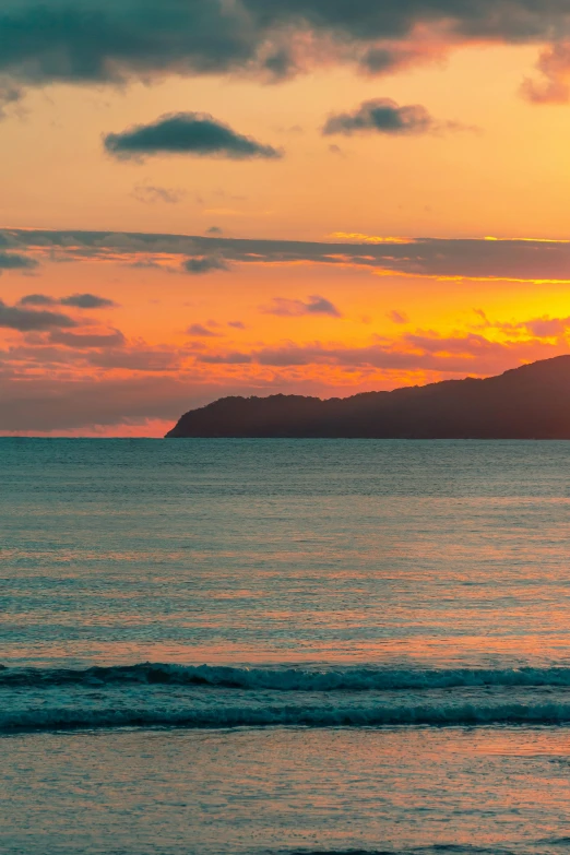 a person riding a surfboard on top of a beach, at the sunset, wellington, sunset in the distance, far view