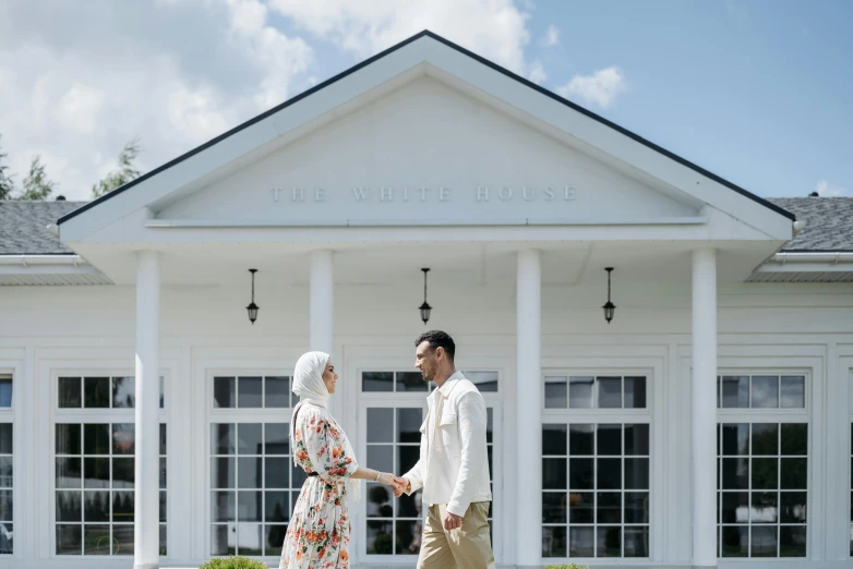 a man and a woman holding hands in front of a building, pexels contest winner, hurufiyya, in front of white back drop, summer season, at the white house, islamic