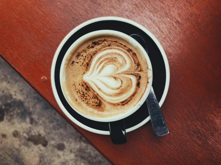 a cup of coffee sitting on top of a wooden table, by Niko Henrichon, trending on unsplash, art nouveau, heart - shaped face, 9 9 designs, fan favorite, latte art