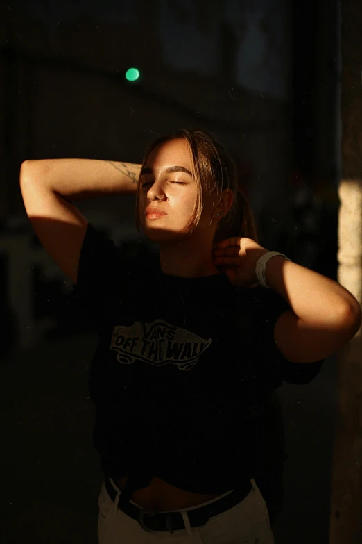 a woman in a black shirt leaning against a wall, inspired by Elsa Bleda, pexels contest winner, happening, sunlight filtering through skin, wearing a tee shirt and combats, evening lighting, teenage girl