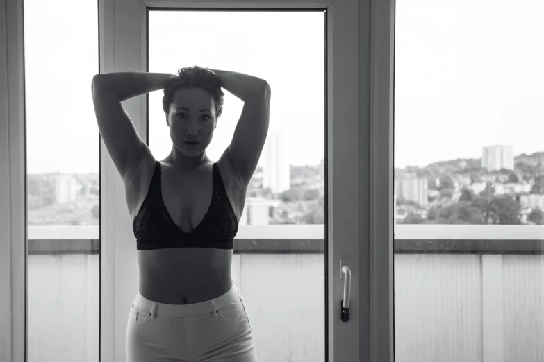 a woman standing in front of a window with her hands on her head, a black and white photo, by Emma Andijewska, unsplash, happening, posing together in bra, curvy build, hotel room, wearing a crop top