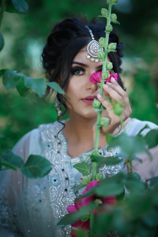 a woman holding a flower in front of her face, by Riza Abbasi, pexels contest winner, arabesque, clothed in vines, wearing an elegant tribal outfit, gorgeous elegant attractive, lights