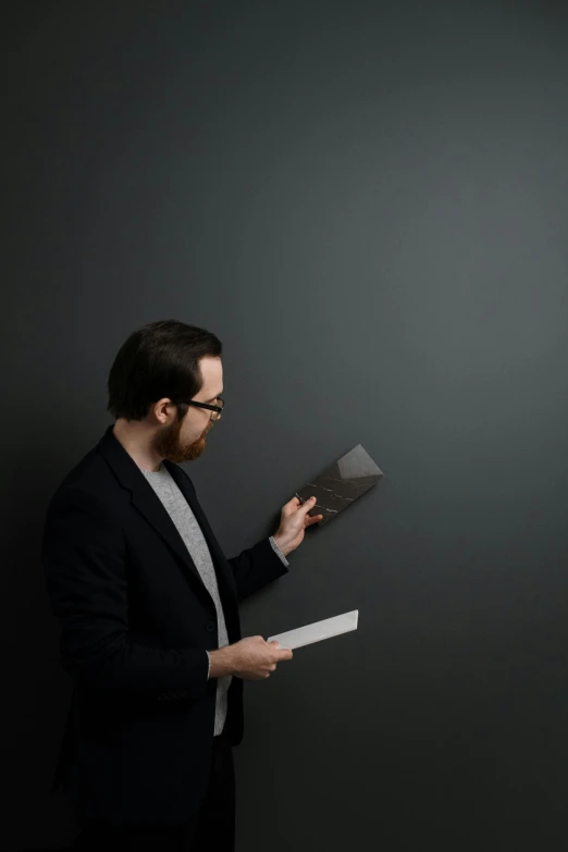 a man in a suit holding a piece of paper, a minimalist painting, unsplash contest winner, darkslategray wall, librarian, looking to the side off camera, light tracing