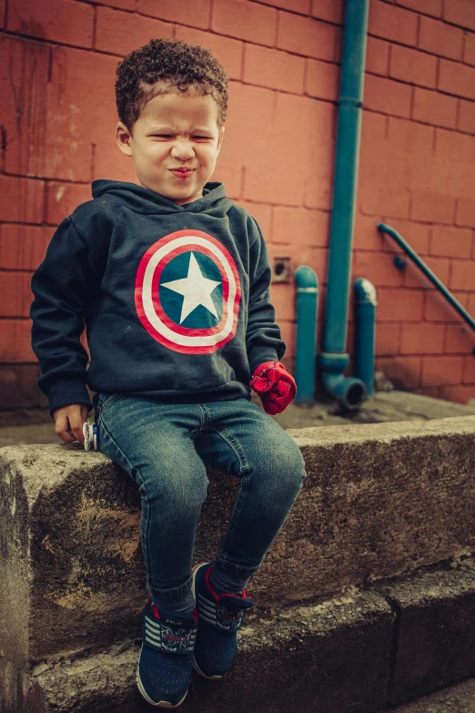 a little boy that is sitting on a ledge, a photo, by Matt Stewart, pexels contest winner, symbolism, captain america, hoodie, slightly smiling, full colour