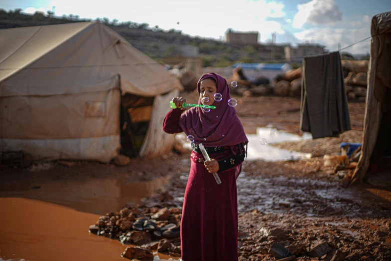 a woman standing in a muddy area next to a tent, hurufiyya, holding a syringe, bubbles, saadane afif, settlement