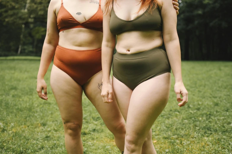 a couple of women standing on top of a lush green field, a colorized photo, trending on pexels, round thighs, obese ), earthy colours, wet swimsuit
