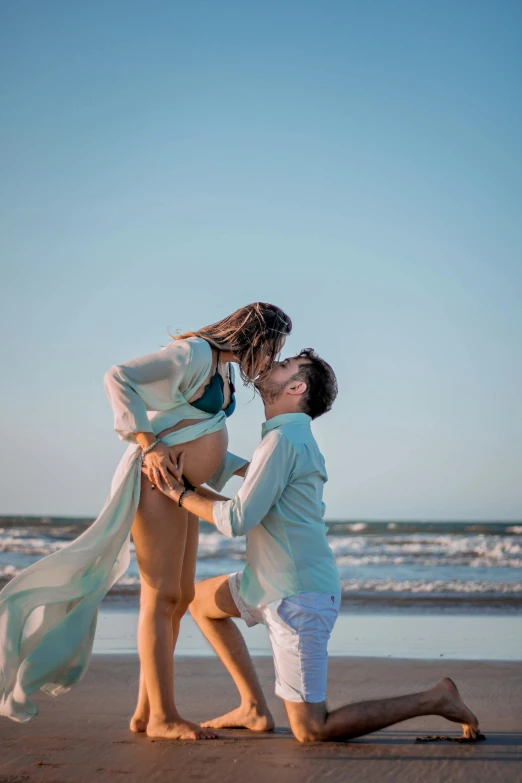 a man kneeling next to a woman on a beach, pexels contest winner, romanticism, pregnant belly, lovely kiss, blue sky, rectangle