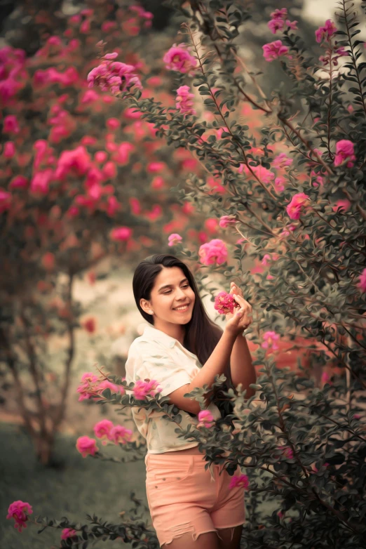 a woman standing in front of a bush of flowers, by Max Dauthendey, pexels contest winner, romanticism, happy girl, indian, roses, medium format. soft light