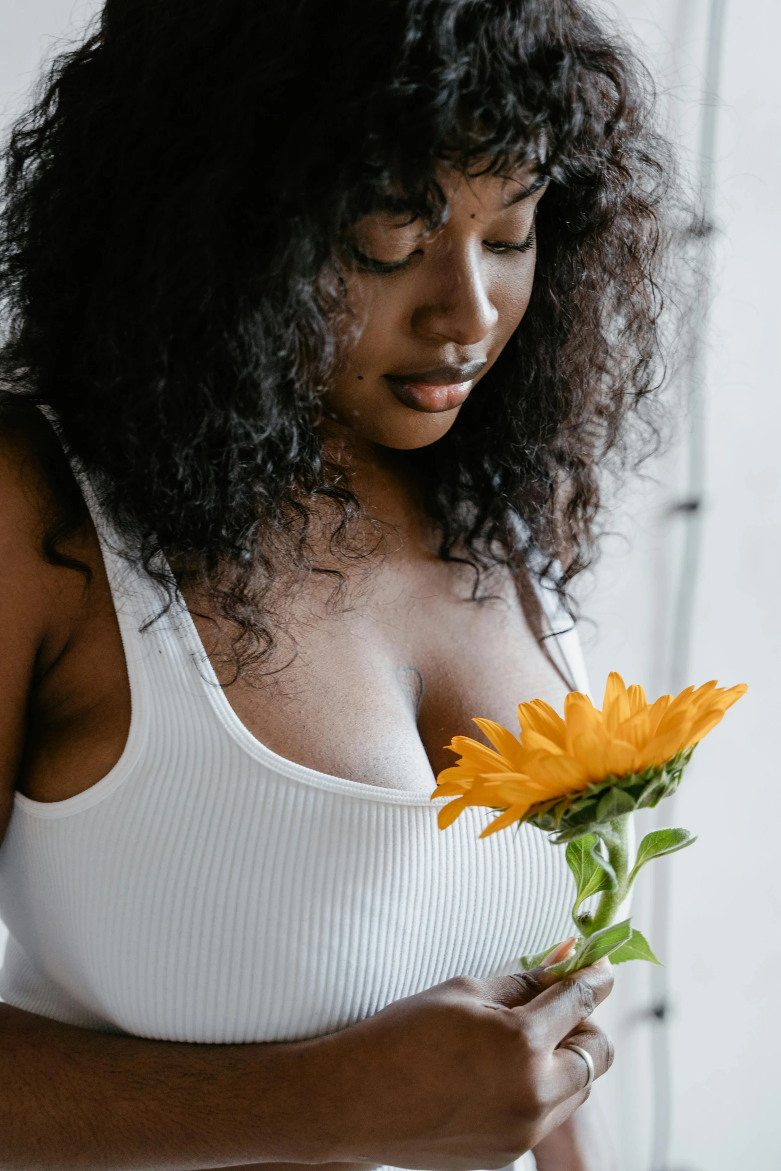 a woman in a white tank top holding a yellow flower, trending on unsplash, with large breasts, dark-skinned, thoughtful ), dressed in a white t shirt