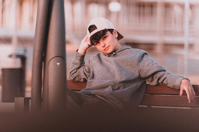 a young man sitting on top of a wooden bench, trending on pexels, realism, wearing a baseball hat, black haired girl wearing hoodie, teen boy, grayish