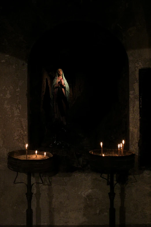 a couple of candles sitting on top of a table, a statue, inside a crypt, during the night