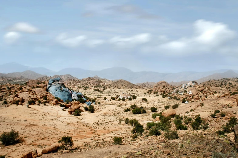 a man riding on the back of a motorcycle down a dirt road, a detailed matte painting, inspired by Scarlett Hooft Graafland, unsplash, hurufiyya, large rocks, somalia, panorama view, conde nast traveler photo