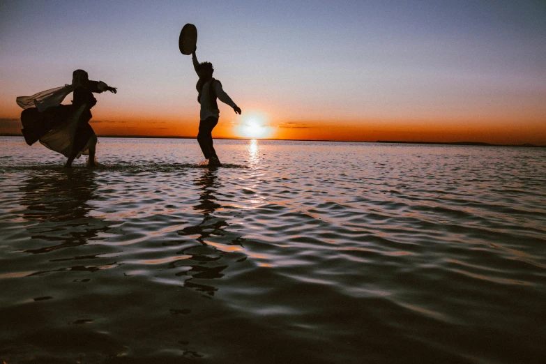 a couple of people standing in the water with a frisbee, by Lee Loughridge, unsplash contest winner, hurufiyya, tribal dance, sun rising, lachlan bailey, performing