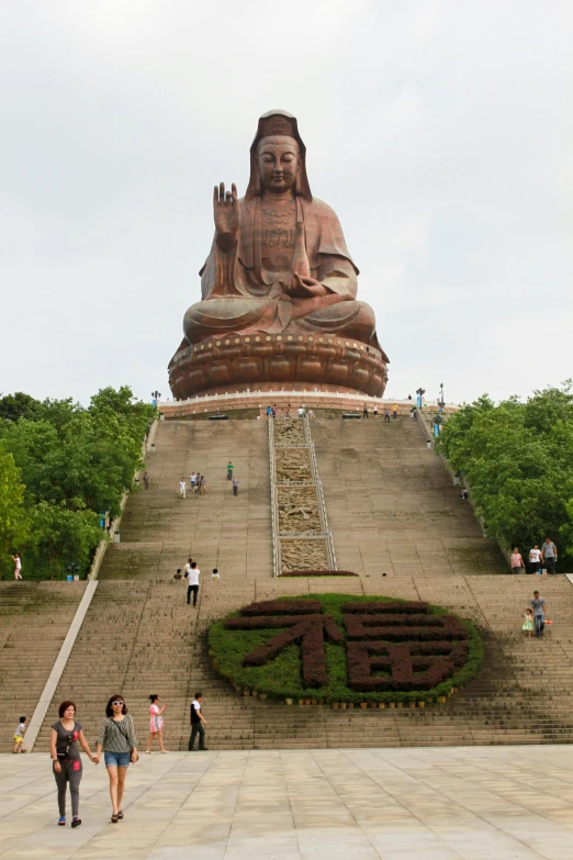 a large statue of buddha sitting on top of a hill, large staircase, female ascending, front facing, king of the hill