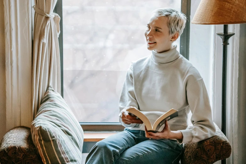 a woman sitting in a chair reading a book, pexels contest winner, short platinum hair tomboy, wearing casual sweater, happy cozy feelings, wearing a turtleneck and jacket